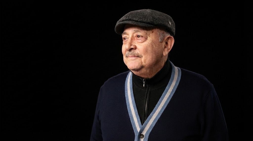 Александр Шаровский — портрет на чёрном фоне, в кепке и тёмном кардигане